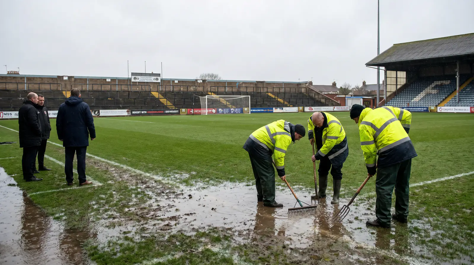 Waterlogged League Two pitch with grounds staff inspecting the surface before kick-off